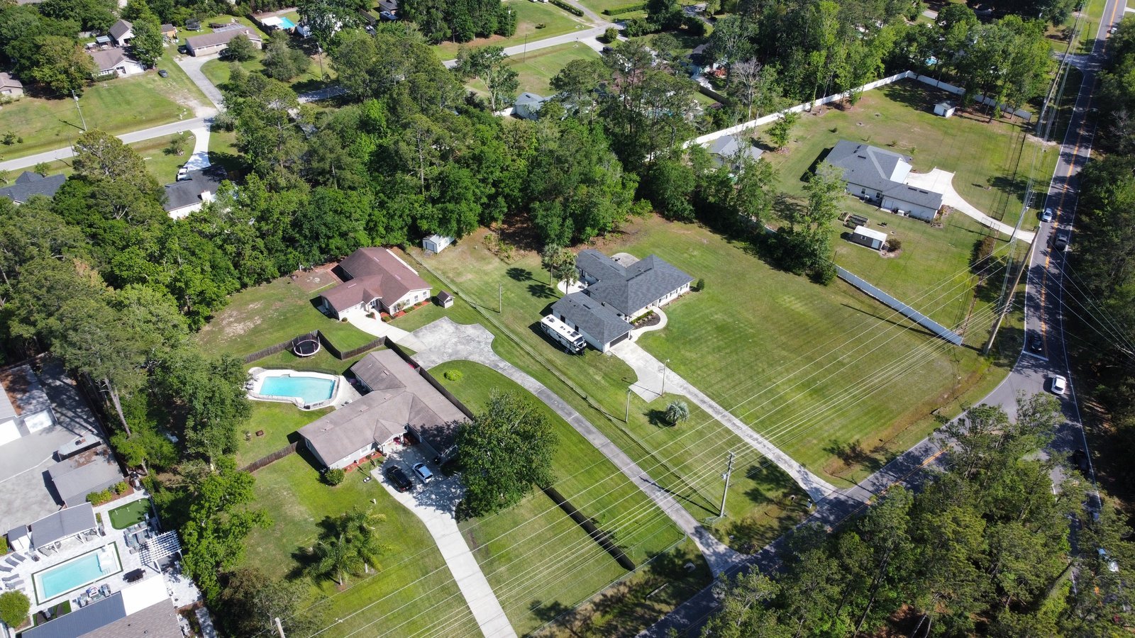 Aerial view of a Fleming Island neighborhood with large green lawns, oak trees, backyard pools and a winding road.